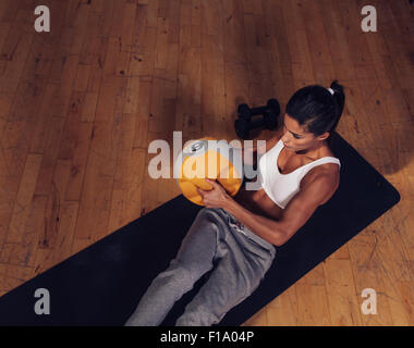 Top view of strong young woman doing core workout using kettlebell weight. Muscular female exercising on fitness mat in gym. Stock Photo
