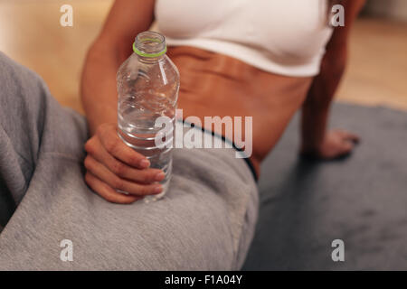 Close-up portrait of fitness woman holding water bottle at gym. Taking a break after training. Stock Photo