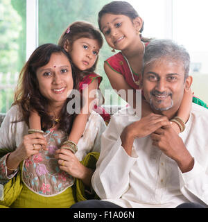 Happy Indian family at home. Asian parents piggyback their children. Adults and kids indoor lifestyle. Stock Photo