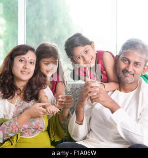 Happy Indian family at home. Asian parents with their kids, sitting on sofa. Parents and children indoor lifestyle. Stock Photo