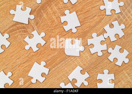 Blank white jigsaw puzzle pieces scattered on wooden table, top view Stock Photo