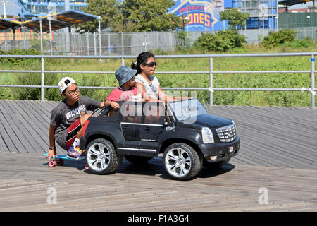 Children driving a miniature electric Cadillac car on the boardwalk in Coney Island, Brooklyn, New York Stock Photo