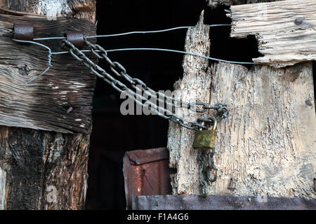An old and worn wooden door partially closed and locked with a chain and a padlock Stock Photo