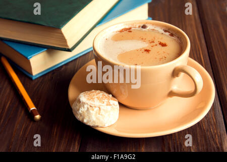 Books and cup of hot cream coffee with cinnamon over rustic wooden table Stock Photo