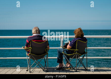 Aberystwyth, Wales, UK. 31st August, 2015.   UK Weather : Two sitting in folding chairs on the promenade enjoying the sunshine on a breezy but warm and sunny Bank Holiday Monday at the seaside in Aberystwyth, on the west wales coast UK   photo Credit:  Keith Morris / Alamy Live News Stock Photo