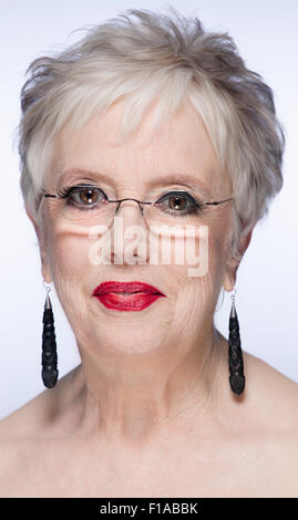 A white European female age 50 plus. The image is a portrait shot in a studio against a grey background. The shot is a head shot Stock Photo