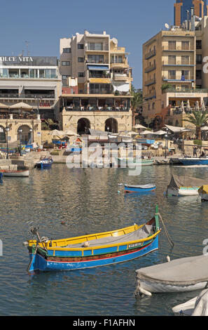 Brightly painted traditional fishing boats with stone buildings beyond, St Julian's Bay, Malta. Stock Photo