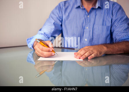 closeup of man sitting at table and writing on a piece of paper Stock Photo