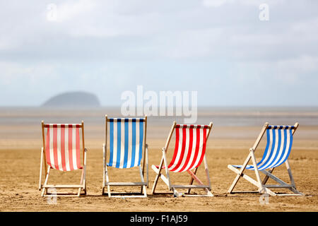A row of striped empty traditional seaside deck chairs waiting for customers on a warm sunny day on a beach in an english seaside resort Stock Photo