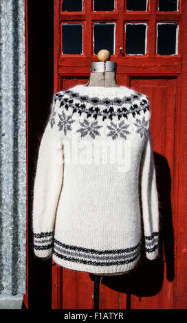 Handmade knitted wool Icelandic sweater with a snowflake pattern with a red door backdrop in Iceland, Europe Icelandic woolens poinsettia pattern Stock Photo