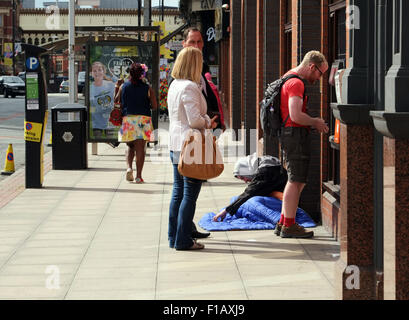 Homeless man sat at the side of a cash point on the streets of Manchester while people queue at the ATM machine. photo DON TONGE Stock Photo