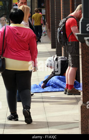 Homeless man sat at the side of a cash point on the streets of Manchester while people queue at the ATM machine. photo DON TONGE Stock Photo