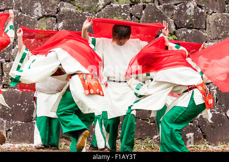 Japanese Yosakoi dance team. Dancers wearing white and green costumes dancing while swirling red cloths. Castle stone wall background.