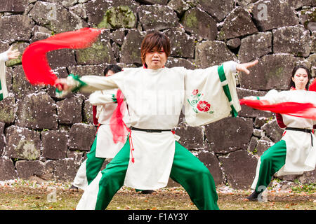 Japanese Yosakoi dance team. Dancers wearing white and green costumes dancing while swirling red cloths. Castle stone wall background.