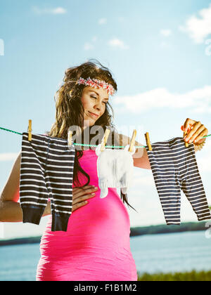 Beautiful pregnant young woman feeling lovely, children clothes on clothesline Stock Photo