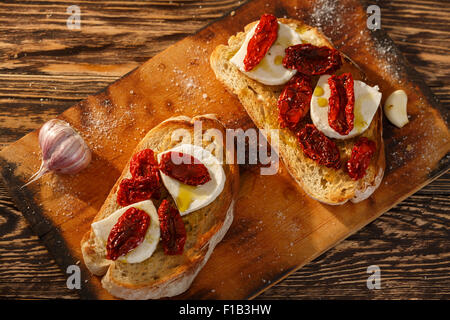 Bruschetta with dried tomatoes, mozzarella, garlic and olive oil. Traditional Italian cuisine sandwich made of grilled ciabatta. Stock Photo