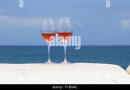 two glasses of rose wine on a whitewashed wall, blue ocean in the background Stock Photo