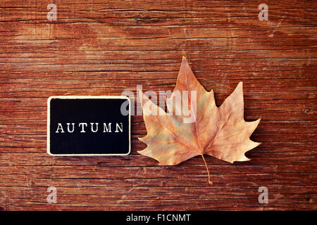 high-angle shot of an autumn leaf and a chalkboard with the word autumn written in it placed on a rustic wooden surface Stock Photo