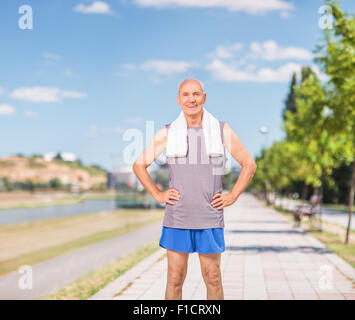 Active senior man in sportswear with a towel around his neck standing on a sidewalk and looking at the camera Stock Photo