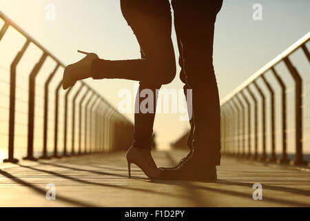 Back light of a couple legs silhouette hugging with love in a bridge at sunset Stock Photo