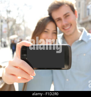 Happy couple or friends making a selfie photo with a smart phone and showing a blank screen to the camera Stock Photo