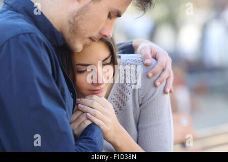 Man comforting his sad mourning friend embracing her in a park Stock Photo