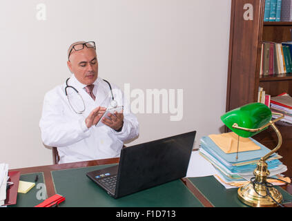 Aback doctor in his studio,  uses a tablet in front of his laptop. Use new technologies. In his professional studio, he is sitti Stock Photo