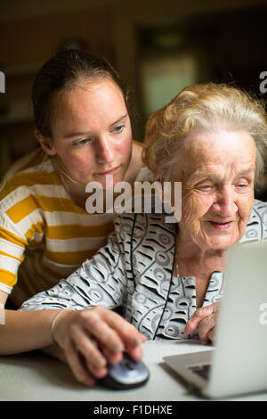 Young girl teaches elderly woman working on the computer. Granddaughter with her grandmother near the computer. Stock Photo