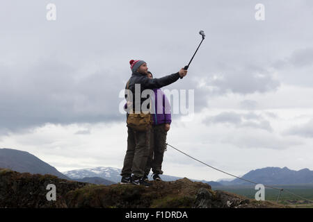 A man and a woman hugging and using a selfie stick to take a picture of themselves in Pingvellir National Park, Iceland Stock Photo