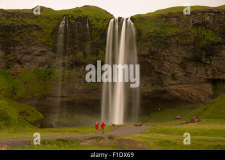 Long exposure shot of Seljalandsfoss waterfall with blurred water and tourists standing at its base - a famous landmark on the south coast of Iceland Stock Photo