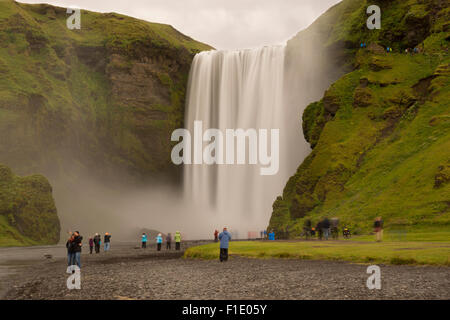 A long exposure of the famous landmark of Skogafoss waterfall on a cold and wet August summer day with tourists below on the south coast of Iceland Stock Photo