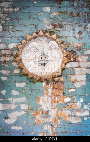Ceramic sun wall decor on painted brick wall Stock Photo