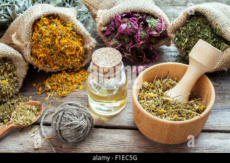 Healing herbs in hessian bags, mortar with chamomile and essential oil on wooden table, herbal medicine. Stock Photo