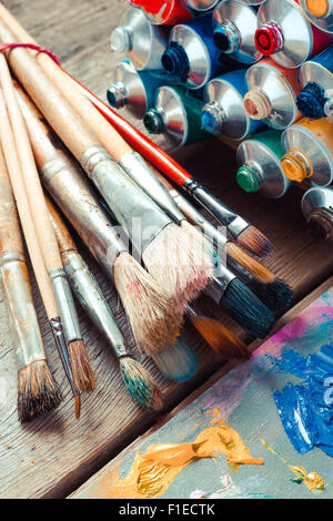 Vintage stylized photo of paintbrushes closeup, open multicolor paint tubes and artist palette. Stock Photo