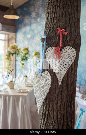 Two wicker hearts hanging on tree in wedding hall. Stock Photo