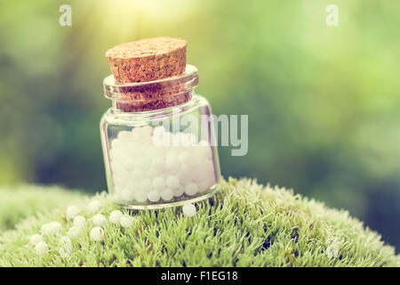 Bottle of white homeopathy globules on green moss. Retro styled. Stock Photo