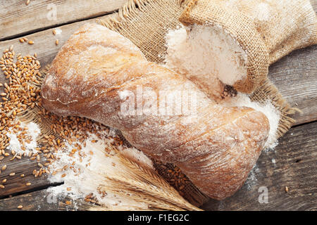 Fresh homemade bread, sack of flour and wheat ears on rustic wooden table. Stock Photo