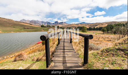 View through footbridge with red boat on lake shore and Drakensberg mountains in the distance Stock Photo