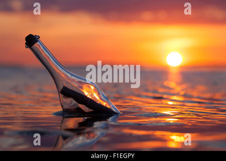 Bottle with a message in the sea at sunset Stock Photo