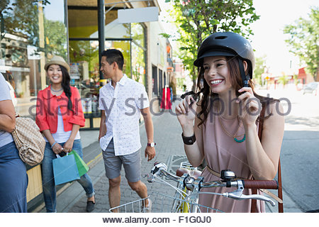 Smiling woman with bicycle putting on helmet