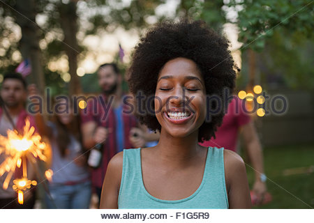 Enthusiastic woman with eyes closed holding sparkler backyard