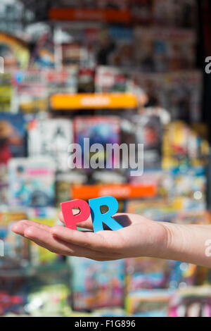 Women hold wooden letters PR. Magazines and newspapers on the background Stock Photo