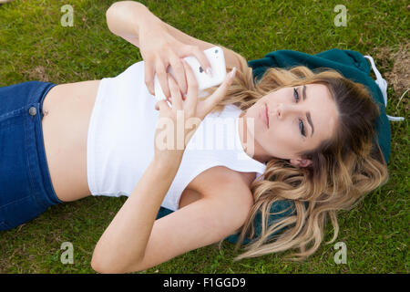 Pretty teenage girl lying down on her back outside using her iPhone. Stock Photo