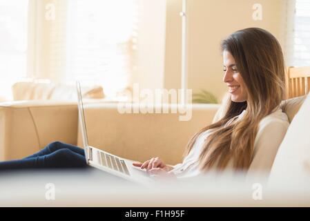 Young woman sitting on sofa, using laptop Stock Photo