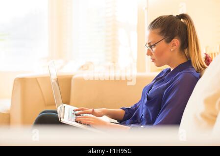 Young woman sitting on sofa, using laptop Stock Photo