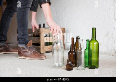 Teenage boy placing empty bottles into wooden crate in garage Stock Photo