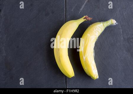 Still life of two bananas - one wrapped in plastic wrap Stock Photo