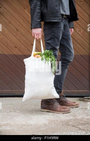 Teenage boy carrying reusable shopping bags full of fresh fruit and veg Stock Photo