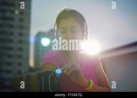 Mature female runner removing MP3 player from armband at dusk Stock Photo