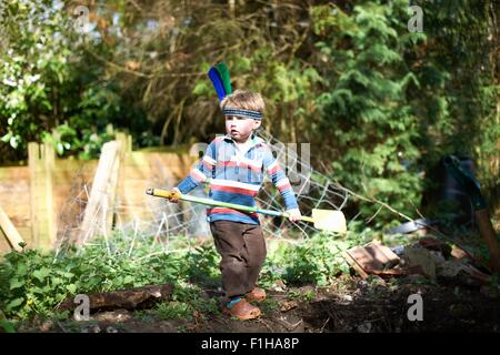 Young boy wearing headband with feathers, holding spade Stock Photo